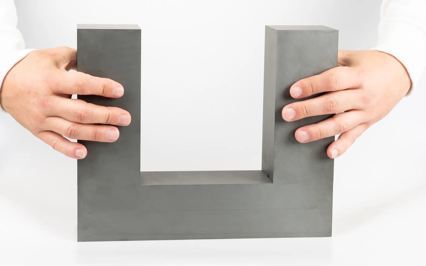 Two hands holding a very large ferrite U-core, showing its physical size